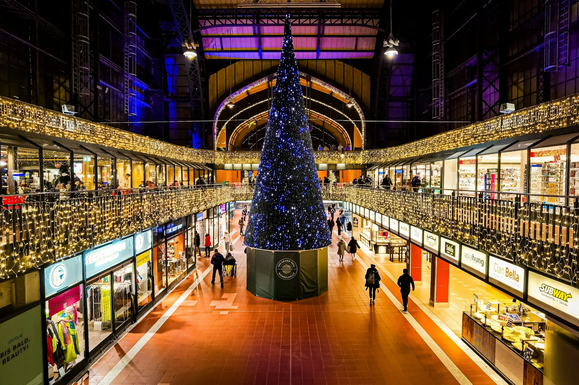 Grand sapin de Noël illuminé au centre d’une galerie marchande