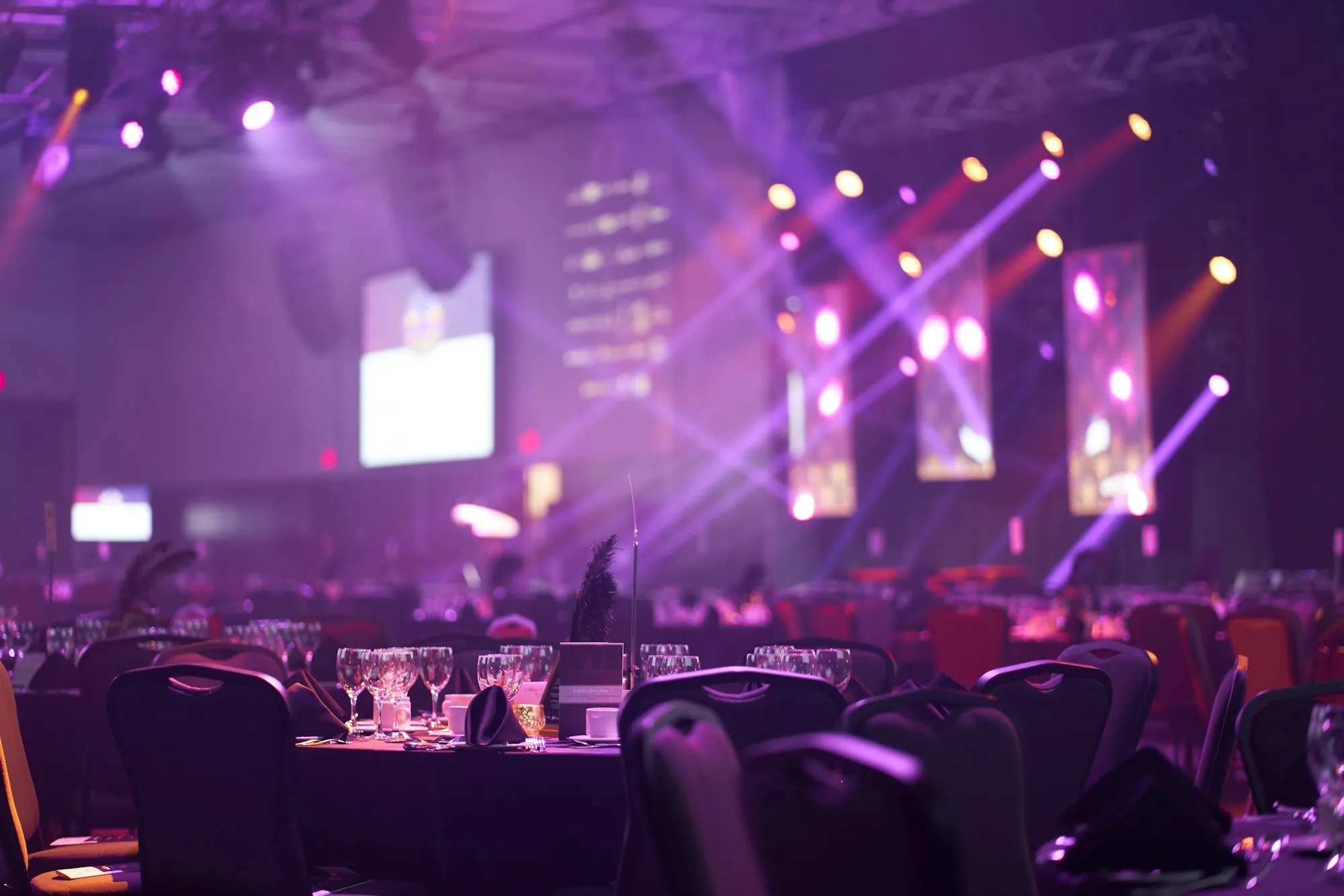 Salle de soirée d’entreprise mise en lumière en violet, tables dressées devant une scène